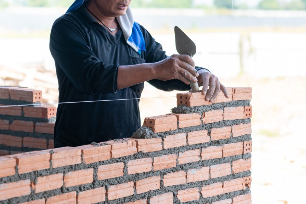 Close up bricklayer worker installing brick masonry on bathroom wall with trowel putty knife in building site.